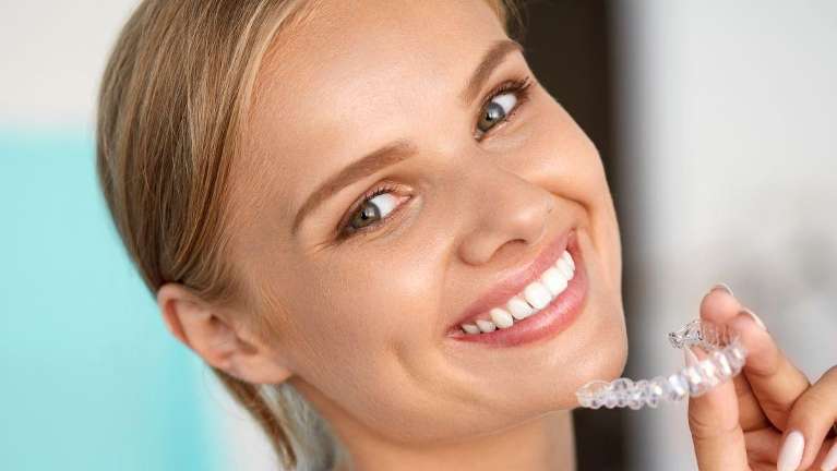 A lady smiling while holding her clear aligners in Mona Vale