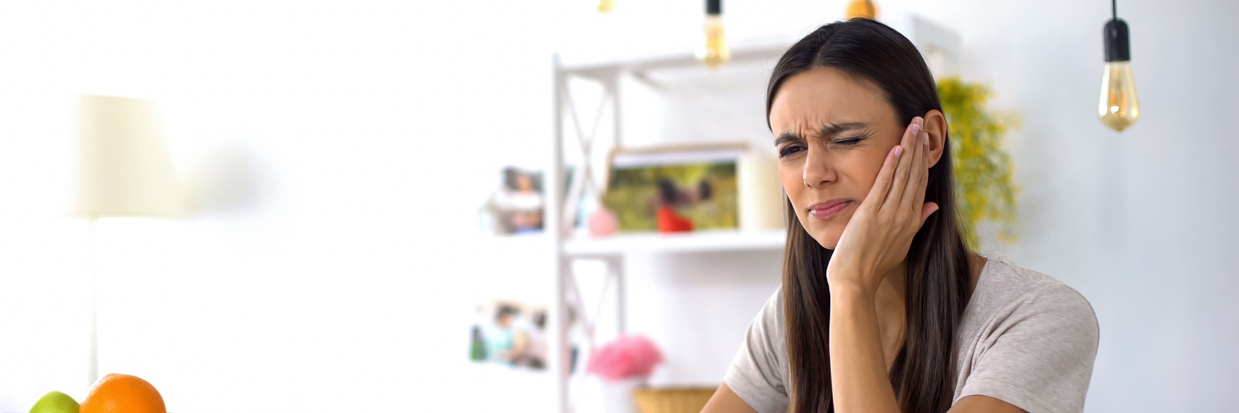 Woman holding her jaw in pain at home, indicating toothache needing root canal treatment